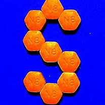 A 3D rendering of the letter "S" made up of small orange hexagons arranged in a hexagonal pattern. The hexagons are evenly spaced and have the letters "S" "B" "C" "D" "E" "F" "G" "H" "J" "K" "L" "M" and "E" written on them in white. The background is a solid blue color. The image appears to be taken from a top-down perspective looking down on the hexagons.