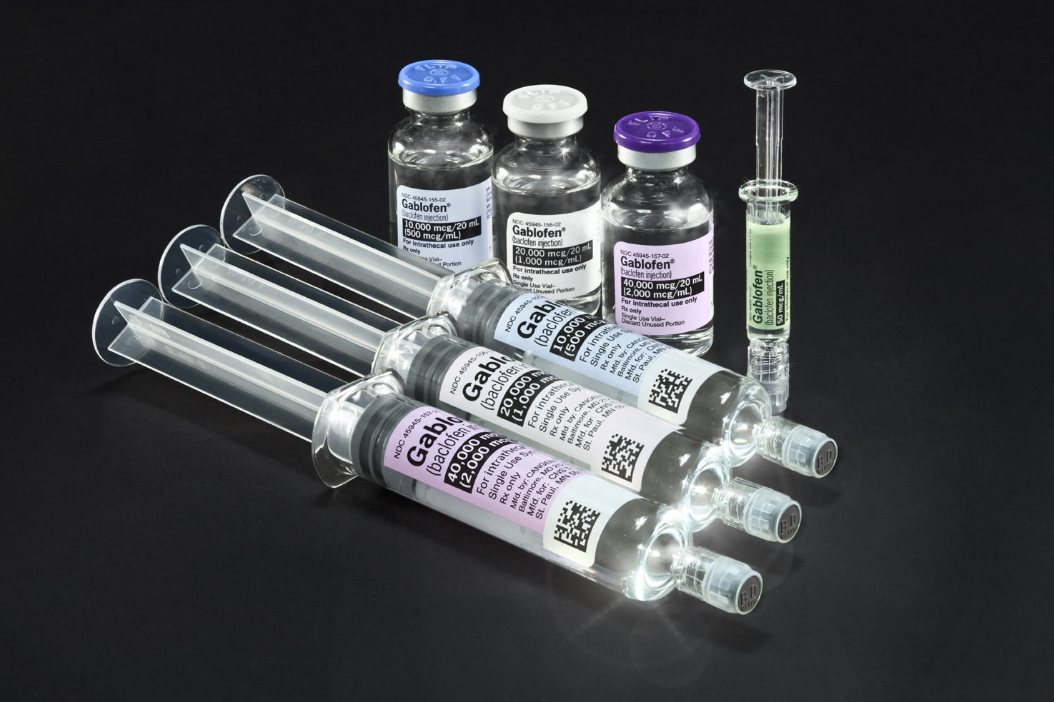 A group of six syringes arranged in a row on a black background. There are six vials of different sizes and shapes each with a blue cap and a white label. The vials are arranged in two rows with the largest one in the center and two smaller ones on either side. The first vial on the left has a purple cap the second vial in the middle has a white cap and the third vial is on the right with a green cap. All the vials appear to be filled with a clear liquid possibly a vaccine or a similar substance.