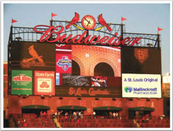 A photograph of Busch Stadium home of the St. Louis Cardinals baseball team. The stadium is a large red brick structure with the word "Budweiser" written in large white letters at the top. Below the word there is a sign that reads "Cardinals" in red letters. On the left side of the image there are several logos of the team's sponsors including Papa John's State Farm and Mallinckrodt Pharmaceuticals. The sign also has a clock and two red birds on it. The sky is blue and there are a few clouds in the background. The image appears to have been taken during the day as the sun is shining brightly.