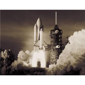 A black and white photograph of a space shuttle taking off from a launch pad. The shuttle is in the center of the image with its nose pointing upwards and its engines roaring as it ascends into the sky. The launch pad is visible in the background with a tall tower on the right side and a large plume of smoke and fire trailing behind it. The sky is dark and cloudy indicating that the photo was taken at night. The image appears to be taken from a low angle looking up at the shuttle as it takes off.