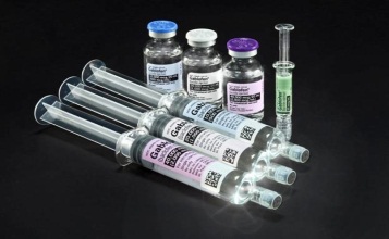 A group of six syringes of different sizes and shapes arranged in a row on a black background. There are six vials of different colors - one with a blue cap another with a purple cap the third with a white cap and the fourth with a green cap. Each vial has a label on it with the brand name "Gastro" written in black text. The vials appear to be filled with a clear liquid possibly a vaccine or a similar substance. There is also a small syringe with a needle on the right side of the image.