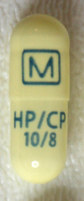 A close-up of a yellow-colored capsule with the letters "M" and "HP/CP" written on it in black. The capsule appears to be made of plastic and has a small hole at the bottom. The letters and numbers on the capsule are written in black and are arranged in a horizontal line. The background is a plain white surface.