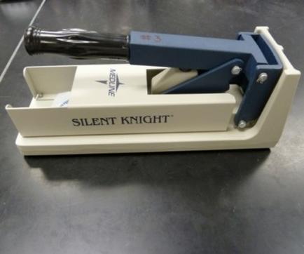 A Silent Knight stapler which is a type of stapling machine used for cutting and shaping materials. It has a white base with the brand name "Silent Knight" written on it in black letters. The top of the base has a blue handle with a black nozzle which can be used to open and close the base. The handle is attached to the base with screws. The base also has a small opening on the right side which allows the user to insert the material into the hole. The staplers are placed on a black surface.