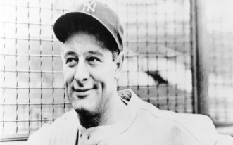 A black and white photograph of a man in a baseball uniform. He is wearing a New York Yankees cap with the team's logo on it. The man is smiling and looking directly at the camera. He appears to be in his late twenties or early thirties. The background is blurred but it seems to be a baseball field with a fence visible behind him. The photograph is likely from the early 20th century.