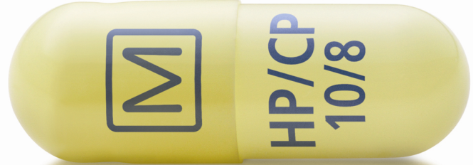 A close-up of a yellow capsule with a blue label on it. The label has the letters "HPCP" and "10/8" written in black. On the left side of the label there is a blue square with the letter "M" in the center. The capsule appears to be made of plastic and has a smooth texture. The background is white.