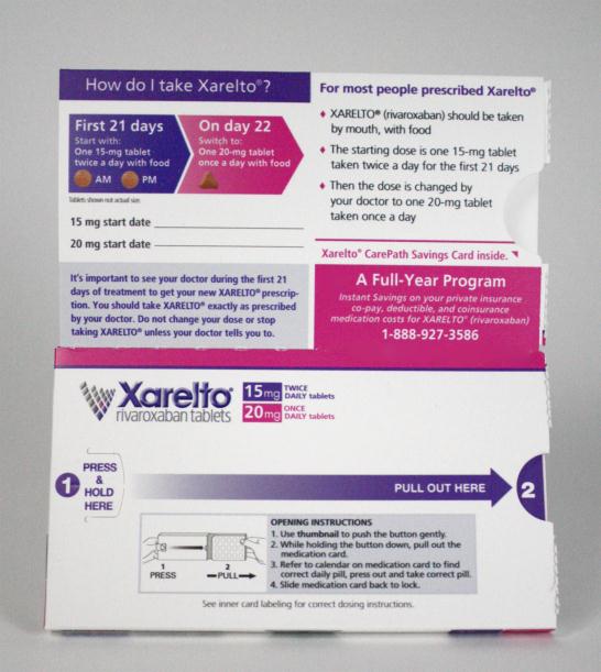 A photograph of a box of Xarelto tablets. The box is white with purple and pink accents. The front of the box has a list of instructions on how to take the tablets. The instructions are written in black text on a white background. <br /><br />The box also has a purple arrow pointing to the right indicating that the user can pull out the instructions. Below the instructions there is a button that says "Pull Out Here" and a link to a full-year program. The label also mentions that the tablets are available for purchase at a discounted price..<br /><br />At the bottom of the label there are two buttons - "Press and Hold" and "Open Instructions".