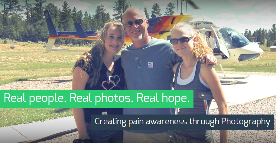 A family of three - a man a woman and a young girl - standing in front of a helicopter. The man is wearing a blue t-shirt and sunglasses and the woman and girl are smiling at the camera. The helicopter is parked on a grassy field with trees in the background. The text on the image reads "Real people. Real photos. Real hope. Creating pain awareness through Photography."