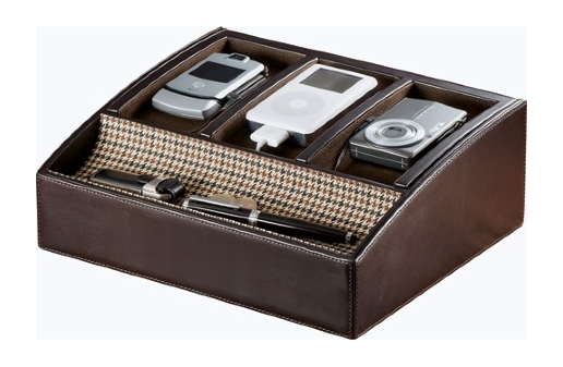 A brown leather desk organizer with three compartments. The compartments are divided into two sections with the top section being the largest and the bottom section being smaller. Inside the compartments there are three items - a cell phone an iPod a camera and a pen. The cell phone is silver in color and appears to be a flip phone. The iPod is white and has a small screen. The camera is silver and is placed on the right side of the compartment. The pen is black and is lying on the bottom left corner of the organizer. The organizer has a houndstooth pattern on the sides.