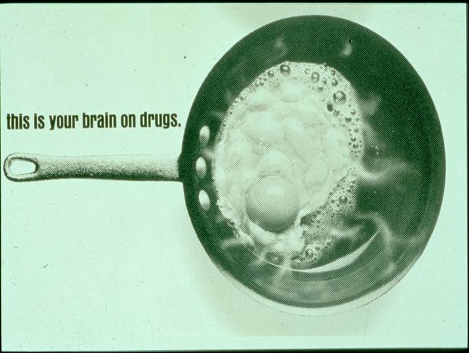 A black and white photograph of a frying pan with a handle. The pan appears to be made of stainless steel and has a round shape with a flat bottom. Inside the pan there is a large oval-shaped object that looks like a brain. The object is covered in small bubbles and bubbles giving it a textured appearance. The background is plain white. The text on the image reads "this is your brain on drugs."