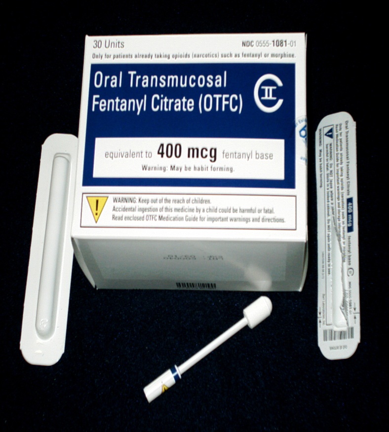 A white box with a blue label that reads "Oral Transmucosal Fentanyl Citrate (OTFC) equivalent to 400 mcg fentanyl base". The box is rectangular in shape and has a handle on the top for easy carrying. On the right side of the box there is a small white tube with a label that says "Warning: Keep out of reach of children. Read this medication guide for important warnings and directions." On the left side there are two white tubes one with a white handle and the other with a yellow handle. The tubes appear to be new and unused. The background is black.