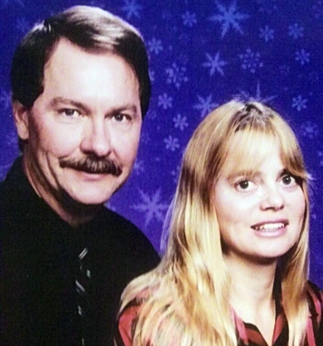 A portrait of a man and a woman. The man is on the left side of the image and the woman on the right side is in the center. They are both smiling and looking directly at the camera. The background is a deep blue color with small white snowflakes scattered across it.<br /><br />The man has a mustache and is wearing a black shirt and tie. He has short dark hair and is looking off to the side with a slight smile on his face. The woman has long blonde hair that is styled in loose waves and is also smiling. She has a red and black striped shirt underneath her shirt. Both of them appear to be in their late twenties or early thirties.