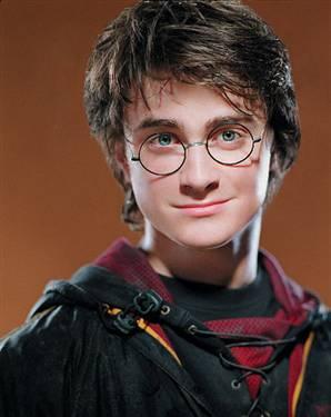 A portrait of a young man who appears to be a character from the Harry Potter series. He is wearing a black robe with a red and gold collar and a pair of round glasses with black frames. His hair is styled in a messy spiky manner and he is looking directly at the camera with a slight smile on his face. The background is a warm orange color making the man the focal point of the image. He has a serious expression on his lips and his eyes are slightly squinted.