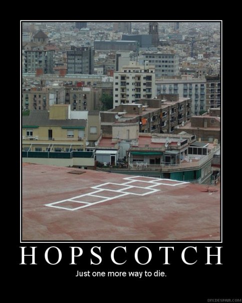 A photograph of a cityscape from a high vantage point. The city appears to be densely populated with buildings of various sizes and colors. The buildings are arranged in a grid-like pattern with some buildings in the foreground and others in the background. The sky is overcast and the overall mood of the image is bleak and desolate. The text on the image reads "Hopscotch - Just one more way to die."