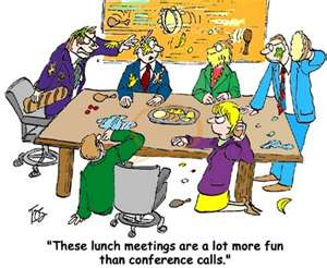 A cartoon illustration of a group of people in a conference room. There are six people in the image three men and three women all dressed in business attire. They are sitting around a large wooden table with plates of food in front of them. The man on the left is wearing a purple suit and tie and is pointing at something on the table while the man in the center is holding a plate of food. The woman on the right is sitting on a chair and appears to be talking on the phone. The other three people are standing around the table and are looking at the man with a concerned expression. The text above the image reads "These lunch meetings are a lot more fun than conference calls."