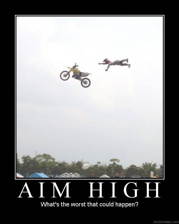 A person on a dirt bike in mid-air performing a trick. The person is wearing a red and white outfit and is in the center of the image with their arms stretched out to the sides. The bike is yellow and black and it appears to be in the middle of a jump. The background is a clear blue sky and there are trees and tents visible in the distance. The text on the image reads "AIM HIGH" and "What's the worst that could happen?"