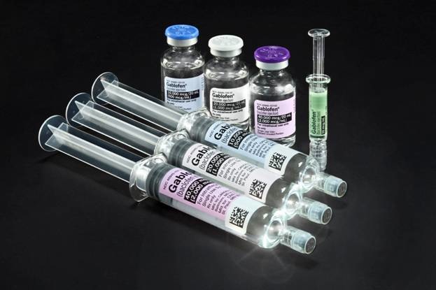 A group of four syringes and three bottles of Gablofen of different sizes and shapes arranged in a row on a black background. All the vials appear to be made of clear plastic (or glass?) and have a cylindrical shape.