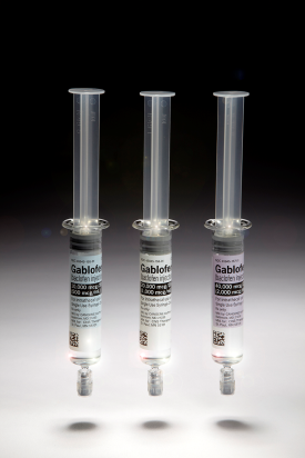 Three syringes of different sizes and shapes. The syringes are arranged in a row with the largest syringe in the center and two smaller syringes on either side. All three syringes have a clear plastic body with a narrow neck and a narrow opening at the top. The label on the syringes read "Gablofen" in bold black letters. The background is black making the syringe stand out. The image appears to be taken in a laboratory setting.