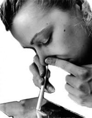 A black and white photograph of a young woman with her eyes closed and her head resting on her hand. She appears to be deep in thought or contemplation. The woman is holding a pen in her right hand and is resting her chin on her left hand. In front of her there is a small piece of paper with the word "love" written on it. The background is plain and the focus is on the woman's face. The overall mood of the image is somber and contemplative.