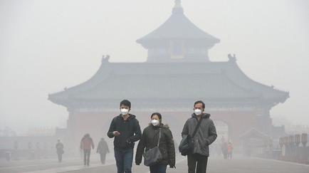 Three people walking in front of a large Chinese temple. The temple is covered in a thick layer of fog obscuring the view of the sky. The people are wearing face masks indicating that they are taking precautions against the ovid-19 pandemic. The sky is hazy and the overall mood of the image is somber.