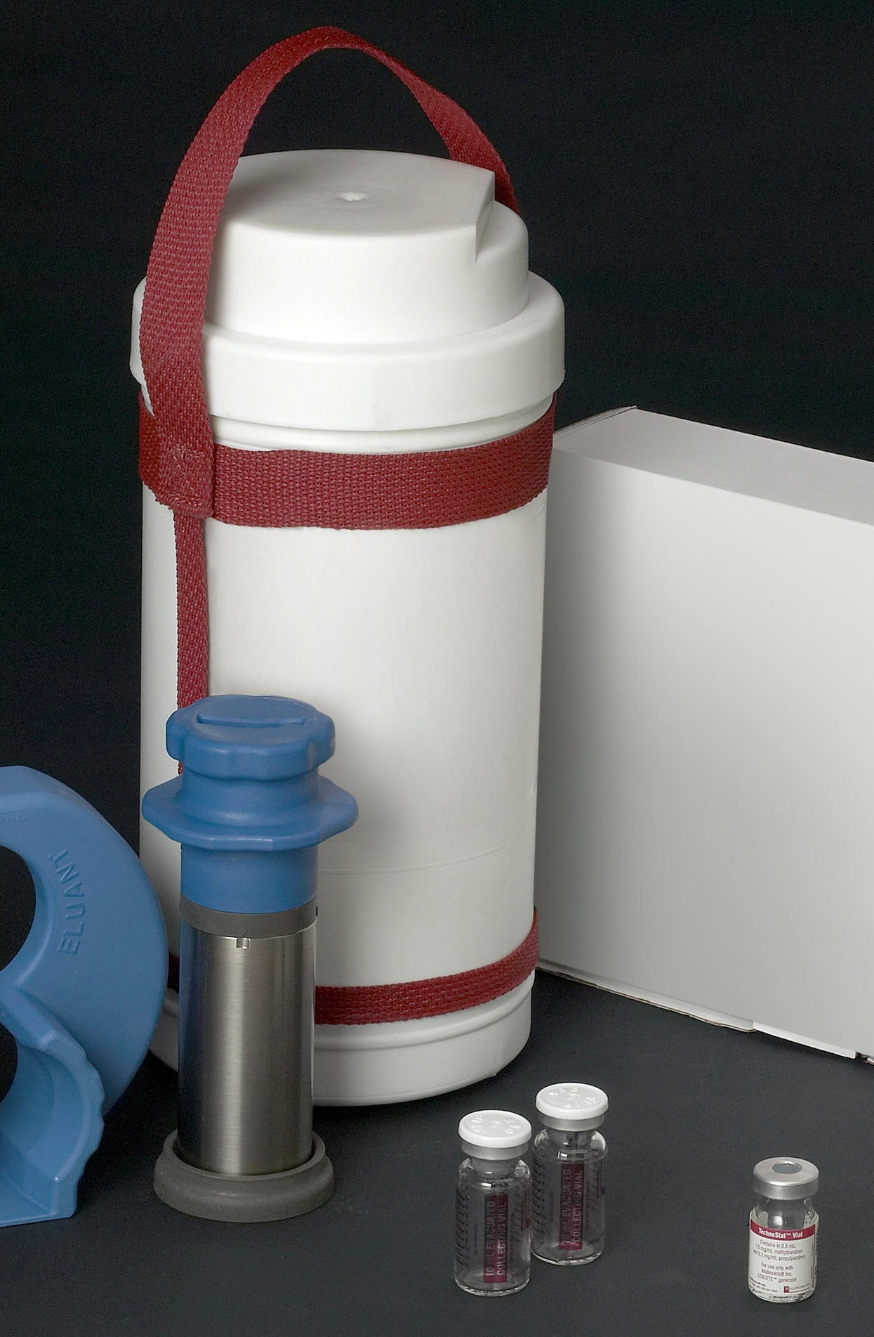 A white cylindrical container with a red strap around the top. The container appears to be made of plastic and has a lid on top. Next to the container there is a blue plastic nozzle with a blue cap. On the right side of the image there are three small glass bottles with white caps. The background is black.