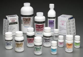 A collection of various types of medicine bottles and containers. There are 12 bottles in total arranged in a scattered manner on a grey background. The bottles are of different sizes and shapes with some being white some being black and some being purple. Some of the bottles have labels on them while others are plain white. There is also a small white box with a label on the left side of the image which appears to be a medicine bottle. The labels on the bottles indicate that they contain different types of medications or supplements. The overall appearance of the items is clean and organized.