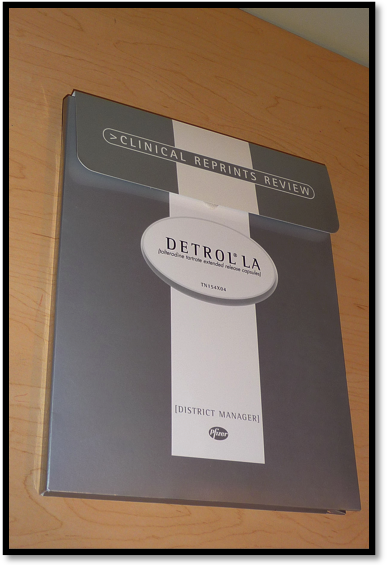 A photograph of a folder with the title Clinical reprints review : Detrol LA (tolterodine tartrate extended release capsules TV15t4X04) for District Managers at Pfizer. The book is lying on a wooden surface. The cover of the book is grey and white with text in white black and gray. The title is written in a bold font and is centered on the cover.