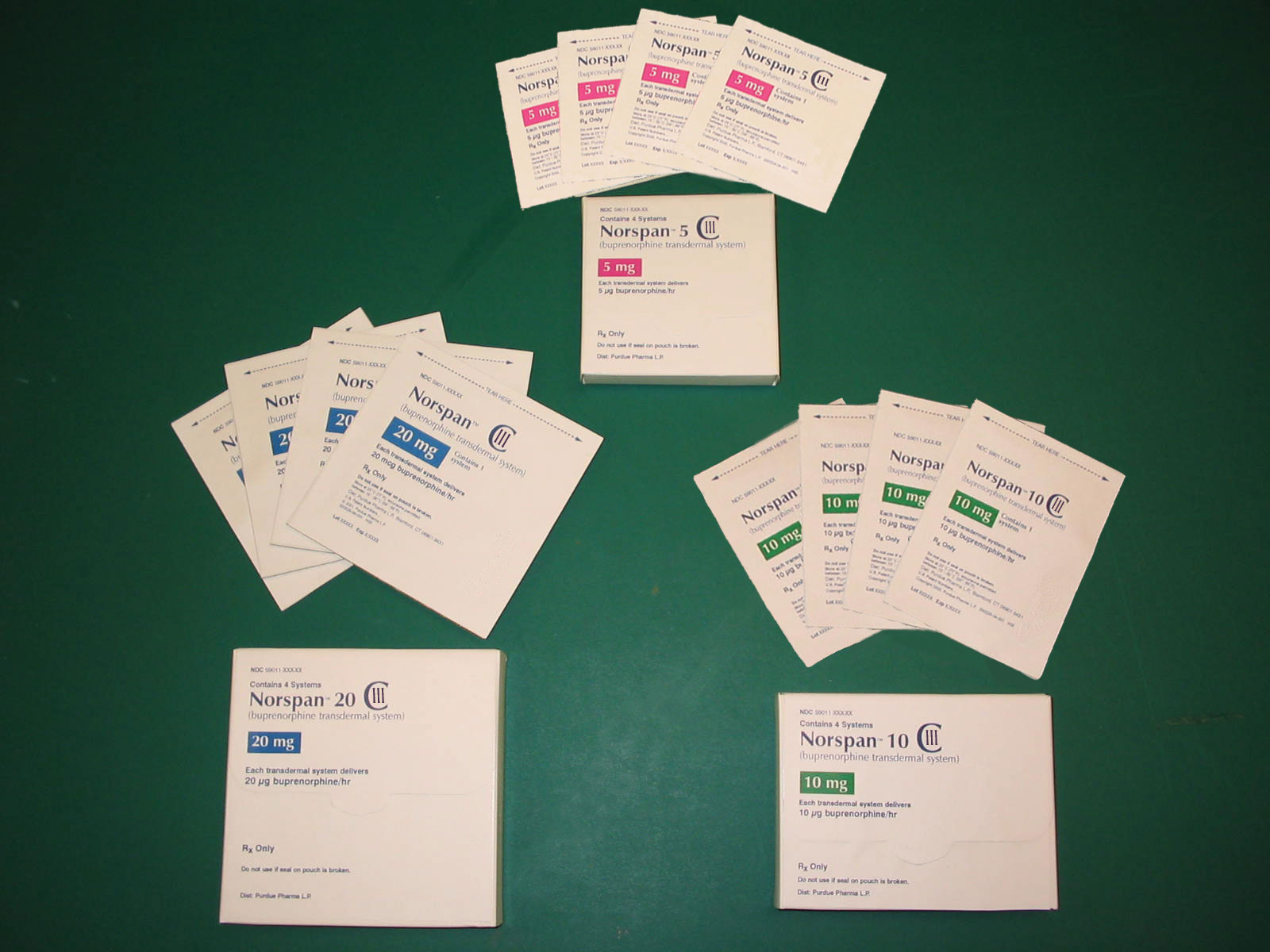 A collection of small white cards scattered on a green surface. There are nine cards in total arranged in a scattered manner. The cards are of different sizes and colors with some being white some being pink and some being blue. Some of the cards have text on them which appears to be instructions or information about the cards. There is also a small white box with a blue label on the bottom right corner of the image. The background is a solid green color.