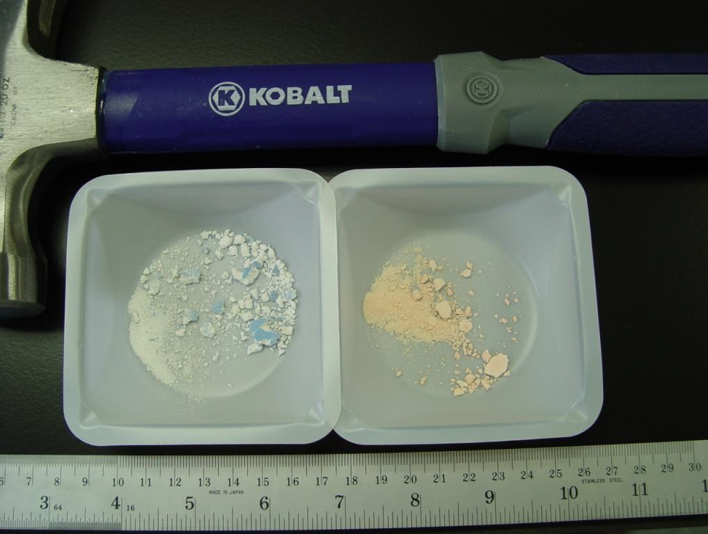 A Kobalt hammer with a blue handle and a silver head. The hammer is resting on a black surface with a ruler next to it. On the left side of the image there is a small white plastic container with two compartments. Inside the compartments there are two small white powder particles one of which appears to be a mixture of white and blue colors. The powder particles are scattered across the surface of the container. The ruler is also visible in the image.