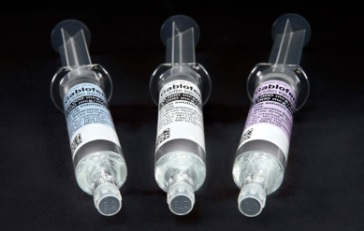 Three syringes of different sizes and shapes. The syringes are clear and have a cylindrical shape with a pointed tip. Each syringe has a label on it and other information about the syringe. The background is black making the syringes stand out.