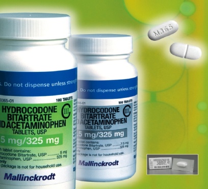 Two white plastic bottles with blue labels. The bottles are labeled "Hydrocodone Bitartrate Acid Acetaminophen Tablets USP" and "5 mg/325 mg". The label also mentions that the tablets contain 5 mg/225 mg and are not for household use. On the right side of the image there are three white pills which appear to be tablets. The background is a light green color with a subtle pattern of circles.