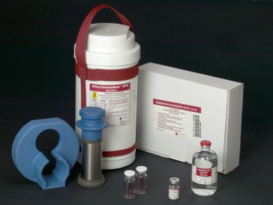 A set of medical equipment including a white container with a red handle and a red strap a white box with a label on it and a blue lid. The container appears to be made of plastic and has a handle on top for easy carrying. Next to the container there are two small vials with red caps one with a blue cap and the other with a silver cap. The vials are filled with a clear liquid and there is a small blue cap on the left side of the container. The background is black and the items are arranged neatly on a surface.