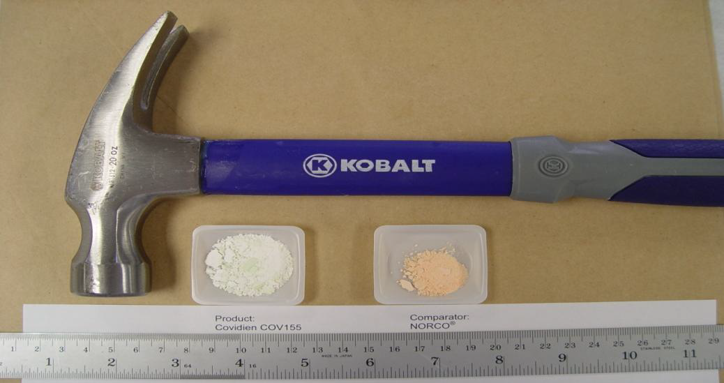 A Kobalt brand hammer with a blue handle and a silver head. The hammer is resting on a beige cardboard sheet. Below the hammer there are two small plastic containers with white powder inside. The containers are labeled "Product: Covidien COV155" and "Comparator: NORCO". A ruler is also visible next to the containers.