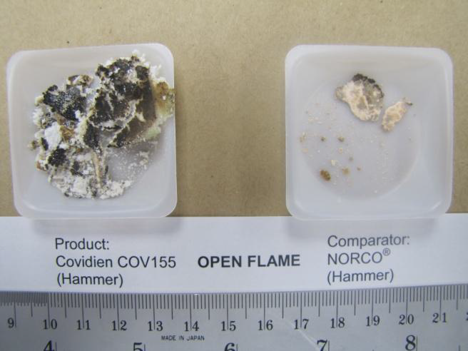 Two small plastic containers one labeled "Product: Covidien COV155 (Hammer)" and the other labeled "Comparator Norco (Hammer)". The containers are placed side by side on a beige background. There is a label beneath both of them that reads "Open flame".<br /><br />On the left side of the image there is a small white container with a black and white substance inside. It has a rough texture and is covered in small bumps and grooves. On the right side the second container has a smaller amount of a similar substance. Both substances look like they are charred.