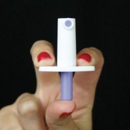 A hand holding a small white and purple device. The device appears to be a small cylindrical object with a pointed tip and a small hole in the center. The person's hand is holding the device with their fingers and their nails are painted with red nail polish. The background is black making the device stand out.