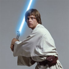 A still from the movie Star Wars: Episode IV - A New Hope. It shows the main character Luke Skywalker holding a blue lightsaber in his right hand. He is wearing a white robe and has a brown belt around his waist. His hair is styled in a messy yet fashionable manner and he is looking off to the side with a serious expression on his face. The background is plain white.