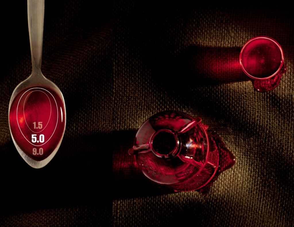 A spoon a glass jar with a lid and a small dosing cup all with red liquid in them presumably a liquid medication. The spoon has a series of circles in them indicating what different dosages look like. The background is black and brown making the red color stand out. The image is taken from above.