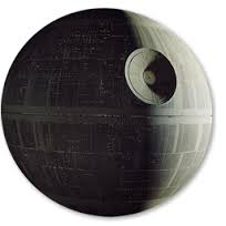 A 3D rendering of the Death Star from the Star Wars franchise. The Death Star is spherical in shape and appears to be made of a black material with a grid-like pattern on its surface. The pattern is made up of lines and dots creating a textured appearance. The background is white making the Death Star stand out.