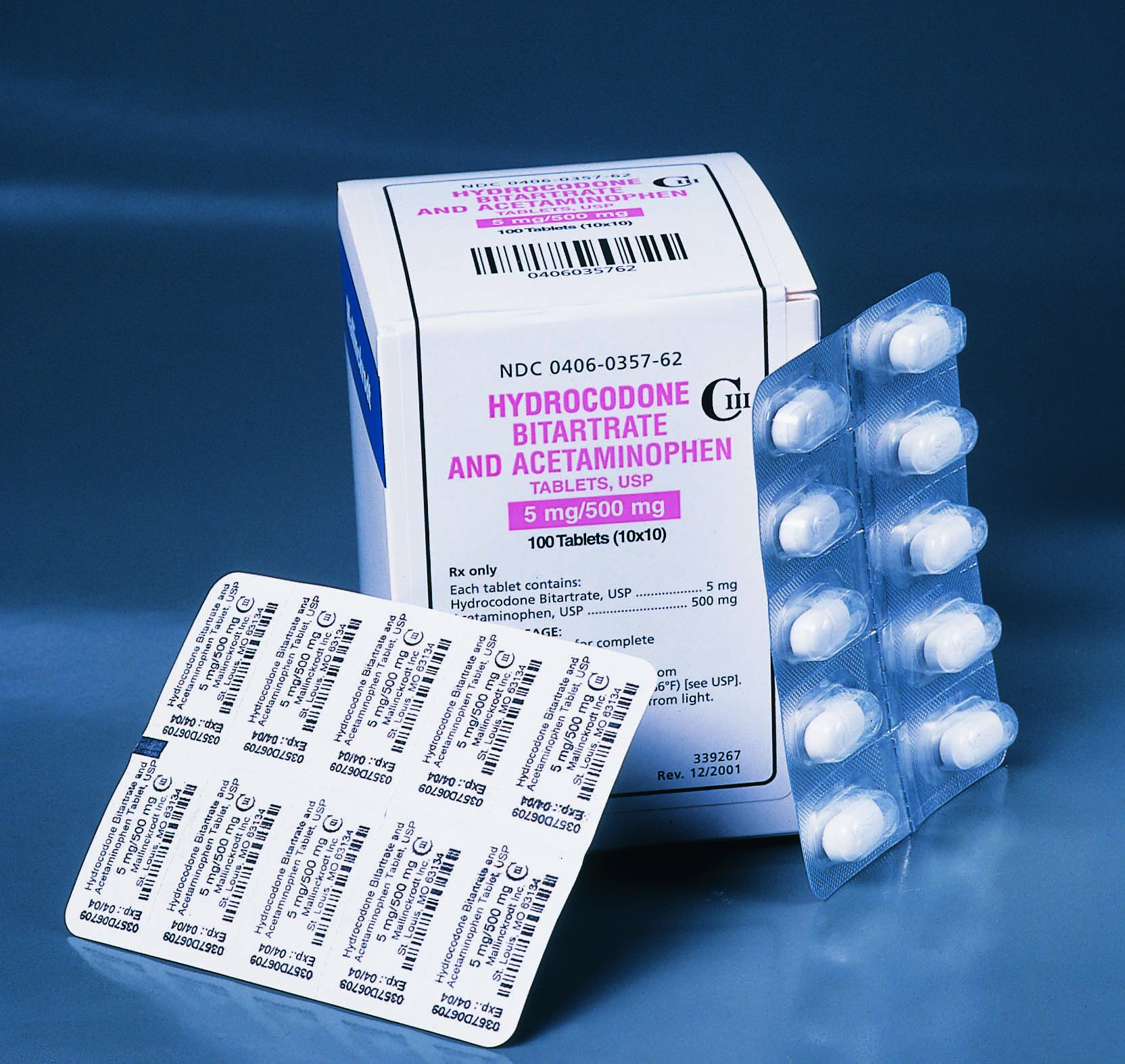 A white box with a blue label that reads "Hydrocodone Bitartrate and Acetaminophen". The box is open and there is a blister pack of the pills next to it. The blister pack is rectangular in shape and has a clear plastic cover. The label also has a barcode and some information about the product. The background is a solid blue color.