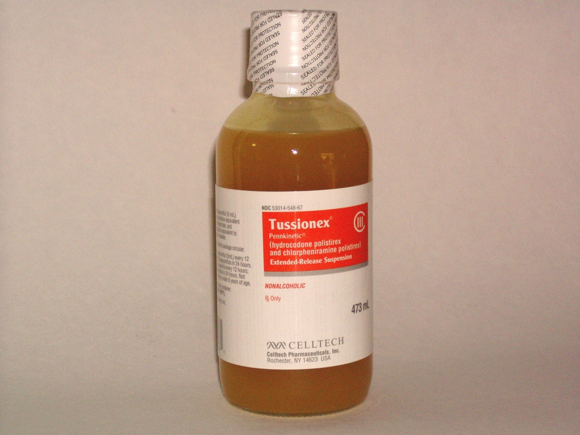 Of a bottle of Tussionex liquid. The bottle is clear and has a white cap with a white and orange label. The label has "Tussionex" written in bold white letters at the top. Below that there is a description of the product which states its main ingredients and is 473 ml in size. The liquid inside the bottle is a light brown color and appears to have a smooth texture. A logo for Celltech is at the bottom of the label.