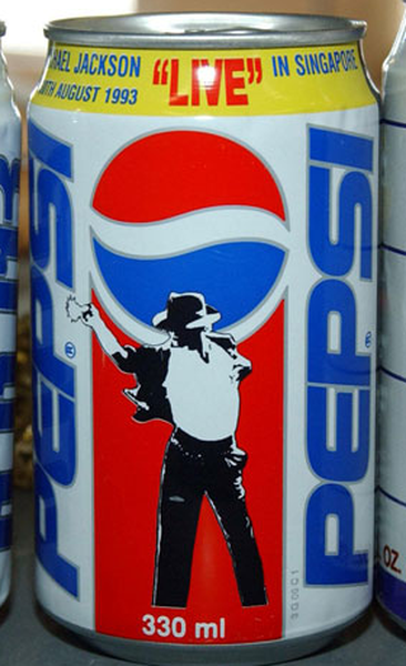 Of a Pepsi can. The can is 330ml in size and has a blue and red color scheme. The top of the can has the Pepsi logo and the words "Live in Singapore" written in white. Below the logo there is an illustration of Michael Jackson the iconic singer and songwriter. He is wearing a white shirt black pants and a black hat. The background of the image is blurred but it appears to be a store shelf with other Pepsi cans visible in the background.