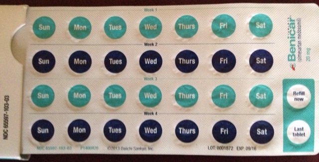 A photograph of a blister pack of Benetton tablets. The blister pack is rectangular in shape and has a white background with blue and green circular labels. The labels are arranged in a grid-like pattern with each label representing a day of the week. The days are written in black text and are numbered from 1 to 12. <br /><br />On the top left corner of the blister pack there is a label that reads "Sun" "Mon" "Tue" "Wed" "Thurs" "Fri" "Sat" and "Last Tablet". On the top right corner there are two labels that read "Refill now". On top of the label there appears to be a label for the last tablet.<br /><br />The blister pack appears to have a label on the bottom right corner with the brand name "Benetton" written in blue text. The label also has a small image of a pill bottle on the right side.