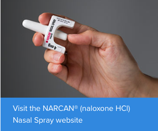 A hand holding a nasal spray device. The device is white in color and has a red and black label on it. The label reads "NARCAN® (naloxone HCI) Nasal Spray website". The device appears to be a small handheld device with a handle on one end and a nozzle on the other end. The nozzle is used to spray the nasal spray onto the skin. The background is plain white.