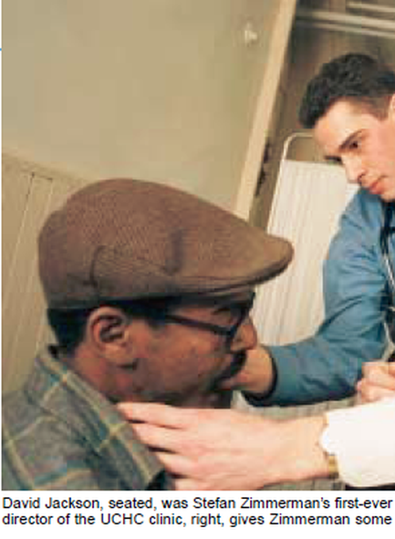 Two men in a room. The man on the left is wearing a brown flat cap and a plaid shirt. He is sitting in a chair with his head resting on the armrest of the chair. The other man is standing next to him wearing a blue shirt and a stethoscope around his neck. He appears to be examining the man's neck. The caption on the image reads "David Jackson seated was Stefan Zimmerman's first-ever director of the UCHC clinic right gives Zimmerman some."