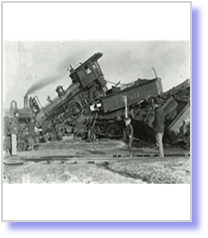 A black and white photograph of a train wreck. The train appears to be a steam locomotive with a large smokestack on the left side and a smaller engine on the right side. The locomotive is tilted to the side with its front end facing towards the viewer. There are several people standing around the wreckage looking at the wreckage. The ground is covered in rubble and debris and there is a pile of rubble in the background. The sky is overcast and the overall mood of the image is somber.