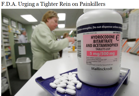 A white bottle of Hydrocodone Bitartrate and Acetaminophen tablets on a blue tray. The bottle has a label that reads "5 mg/500 mg" and "Mallinckrodt". In the background there is a woman in a green jacket working in a pharmacy. She appears to be urging a tighter rein on painkillers.