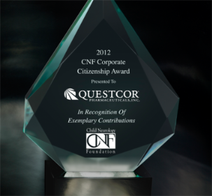 A photograph of a glass award. The award is in the shape of a diamond and is displayed on a black base. The glass is transparent and has a glossy finish. On the front of the award there is a black background with white text that reads "2012 CNF Corporate Citizenship Award Presented to QUESTCOR Pharmaceuticals Inc. In Recognition of Exemplary Contributions." Below the text there are two logos - one for the CNF Foundation and the other for the organization.