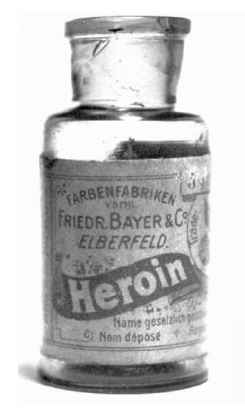 A black and white photograph of a small glass jar with a metal lid. The jar appears to be made of glass and has a label on it that reads "Farbenfabrikken Frieder Bayer & Co. Elberfeld Heroin". The label also has some text written in German which translates to "Heroin" in English. Below the text there is a label that says "Name gesetzlich" which is German for "Non depose". The jar is likely used for storing and dispensing heroin.