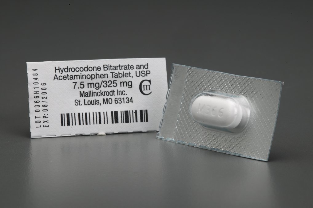 A small rectangular blister pack with a white label on it. The label has the text "Hydrocodone Bitartrate and Acetaminophen Tablet USP 7.5 mg/325 mg" and a barcode on the left side. On the right side of the blister pack there is a small white pill with the number "V365" printed on it which appears to be a medication. The blister pack is placed on a grey surface.