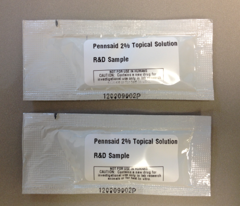 Two rectangular plastic packets with a white label on them. The label reads "Pennsaid 2% Topical Solution R&D Sample". The packets appear to be sealed and are placed on a beige surface. The text on the labels is written in black and is in a clear plastic font. The packets are rectangular in shape and have a glossy finish.