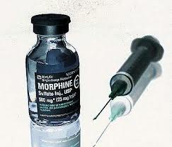 A small glass vial with a black cap and a label that reads "Morphine Sulfate Injection USP 500 mg/ml". Next to the vial there is a syringe with a needle inserted into it. The syringe is filled with a clear liquid which appears to be a type of injection. The background is white and the syringe and vial are placed side by side.